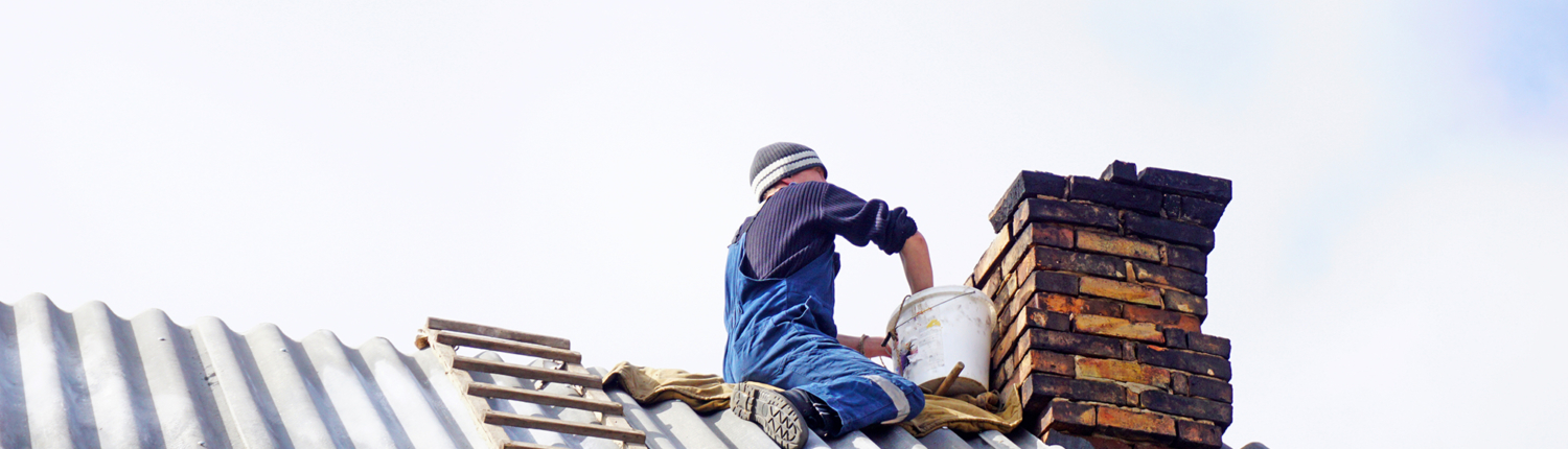 man on metal roof applying mortar to masonry chimney