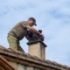 Picture of a person on top of a roof, inspecting the inside of a chimney.