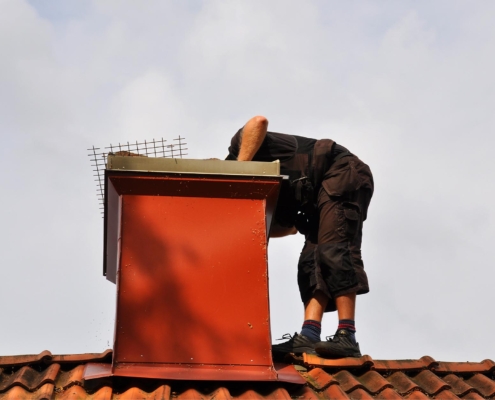 Image of a worker inspecting a chimney from the top of a roof.