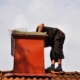 Image of a worker inspecting a chimney from the top of a roof.