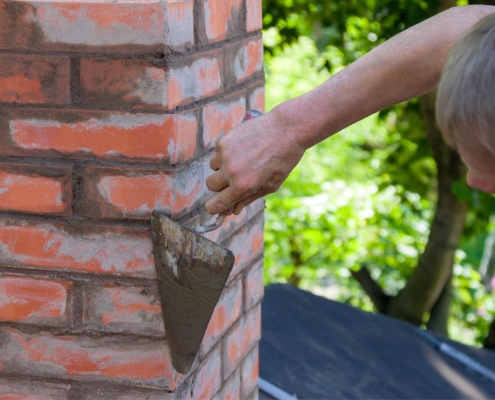 Image of a worker tuckpointing a residential chimney.
