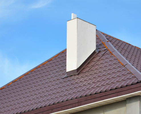 Close-up on a dark red metal tiled bonnet roof with a white chimney