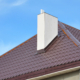 Close-up on a dark red metal tiled bonnet roof with a white chimney