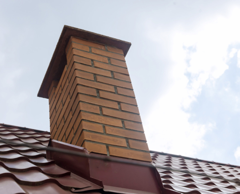 Worms eye view of an orange brick chimney on a red clay tile roof